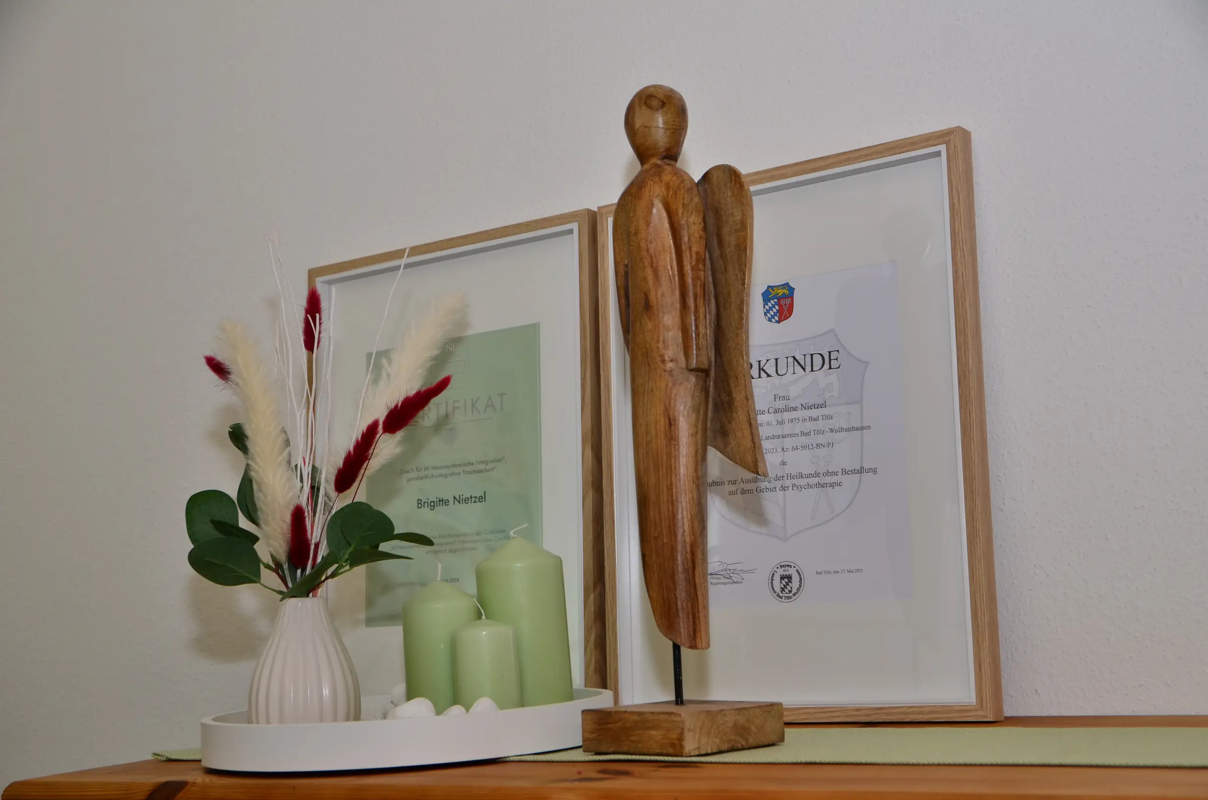 Blumenschmuck und ein Holzengel steht vor 2 gerahmten Zertifikaten